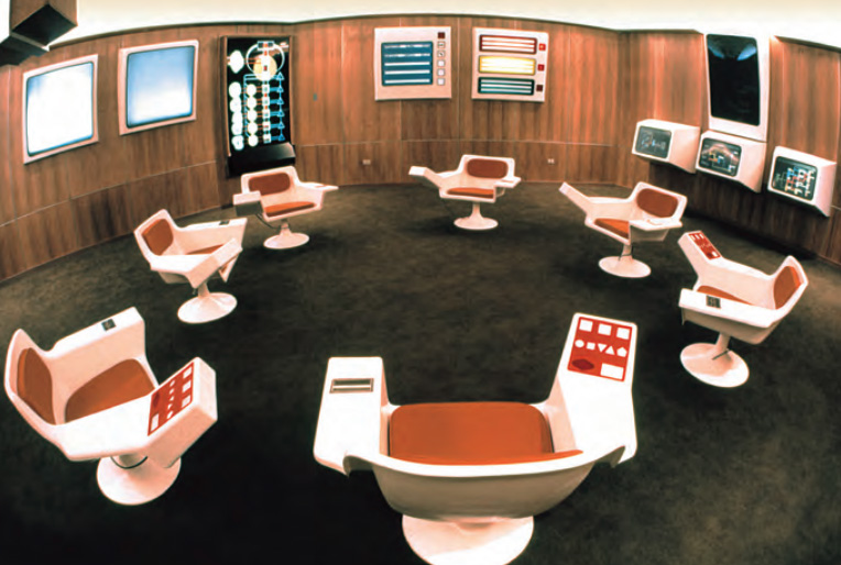 The original Cybersyn operations room in 1973: white swivel chairs in a ring facing wall screens.